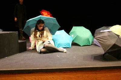 Emily Swora sits under an umbrella on the Umble Center stage, where umbrellas are scattered across the stage