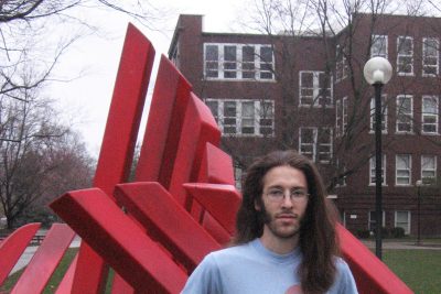 Jeff Stoesz stands in front of the campus "Shield" sculpture