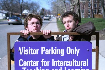 Michael Martin and David Kempf make sad faces behind a "Visitor Parking Only" sign