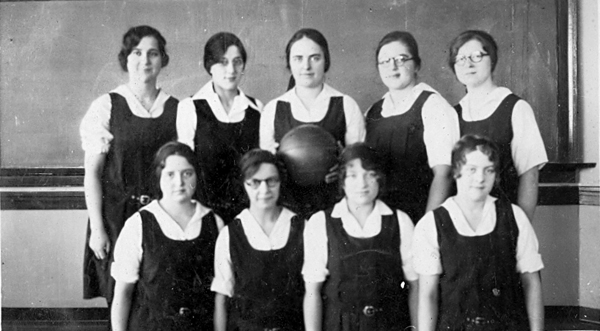 Black and white image from the Mennonite Church USA Archives of a group of nine women in school uniforms standing in front of a chalkboard