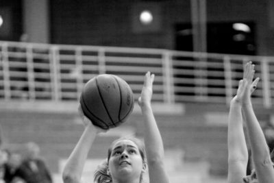 Black and white image of Jenna Rusmisel handling the ball during a game. She is wearing a number "20" Goshen College jersey