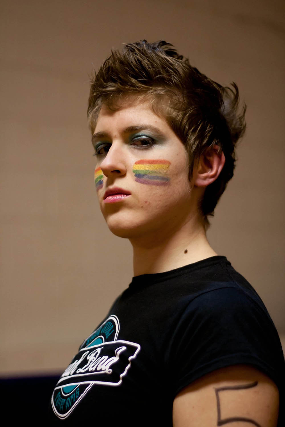 Portrait of Charlotte Barnett. Barnett's face is painted with two rainbow pride flags