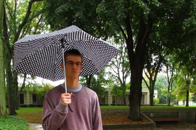 John Miller stands under an umbrella in the rain in Schrock Plaza