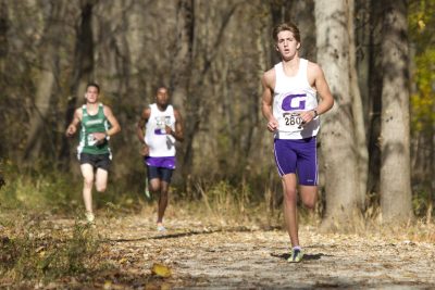 Two Goshen College runners race at a cross country meet. A runner from an opposing team races against them through the woods