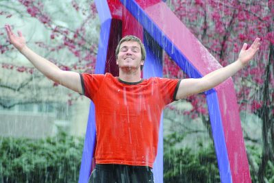 A student enjoys a rainstorm in front of a sculpture on campus