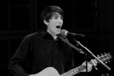 Nathaniel Tann plays guitar and sings into a microphone