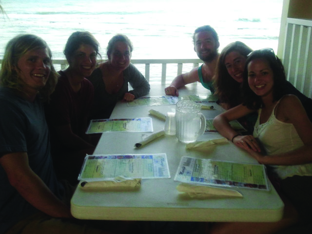 Sara Alvarez, her five friends, and her grandmother sit in a Puerto Rican restaurant booth with the ocean in the background