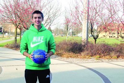 Diego Zago wears a neon green "Nike" hoodie and holds a soccer ball on the Goshen College campus