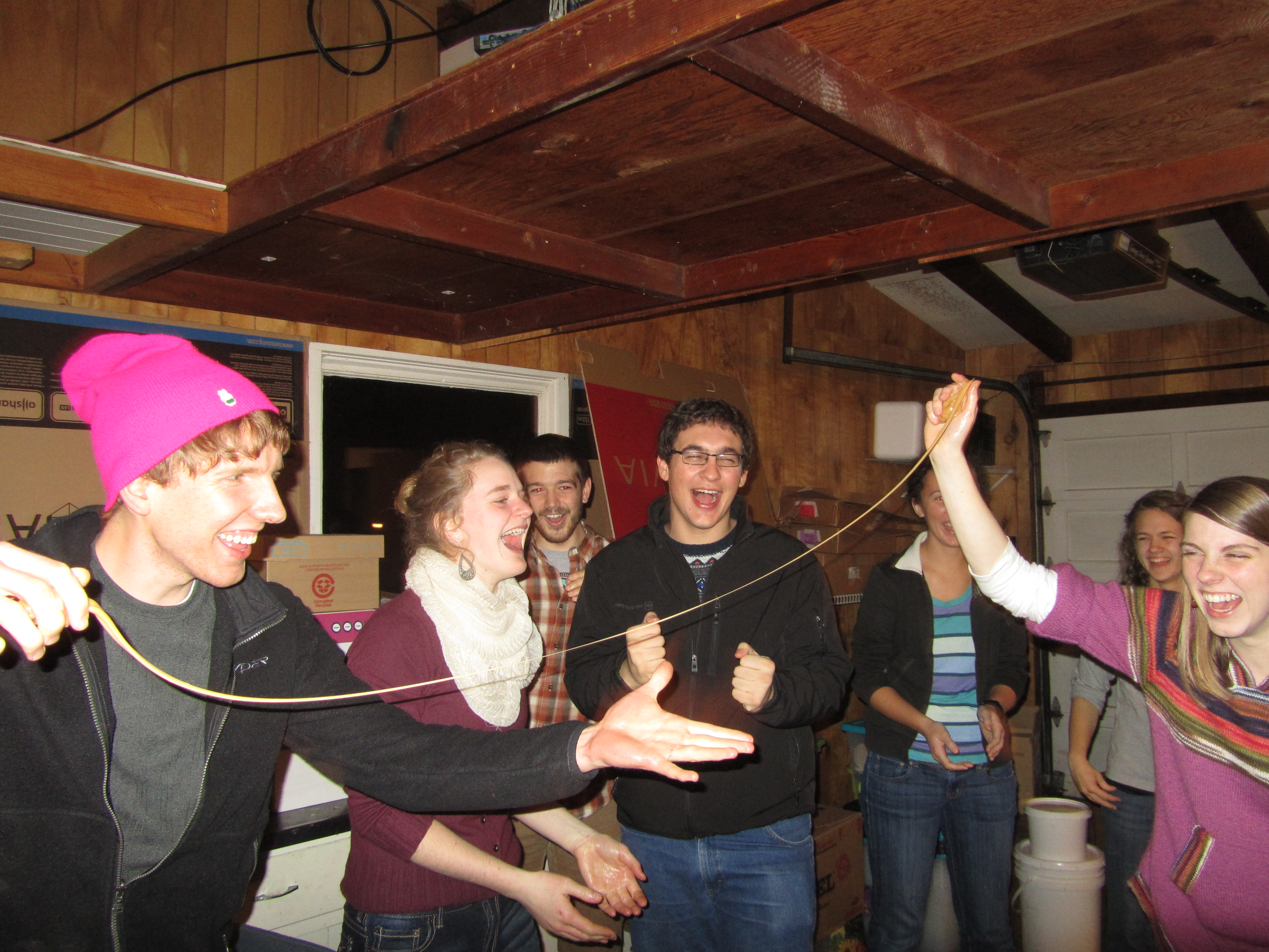 Seven students participate in a campus taffy pull at Vita House. Two students pull a taffy while the others cheer them on