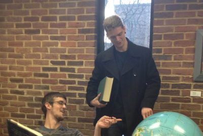 Funnies editors John and Brian point at a large globe in the Good Library