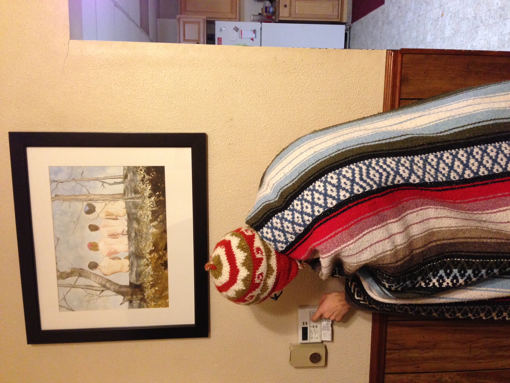 Josh Yoder adjusts the Prude House thermostat while wearing a warm hat and blanket