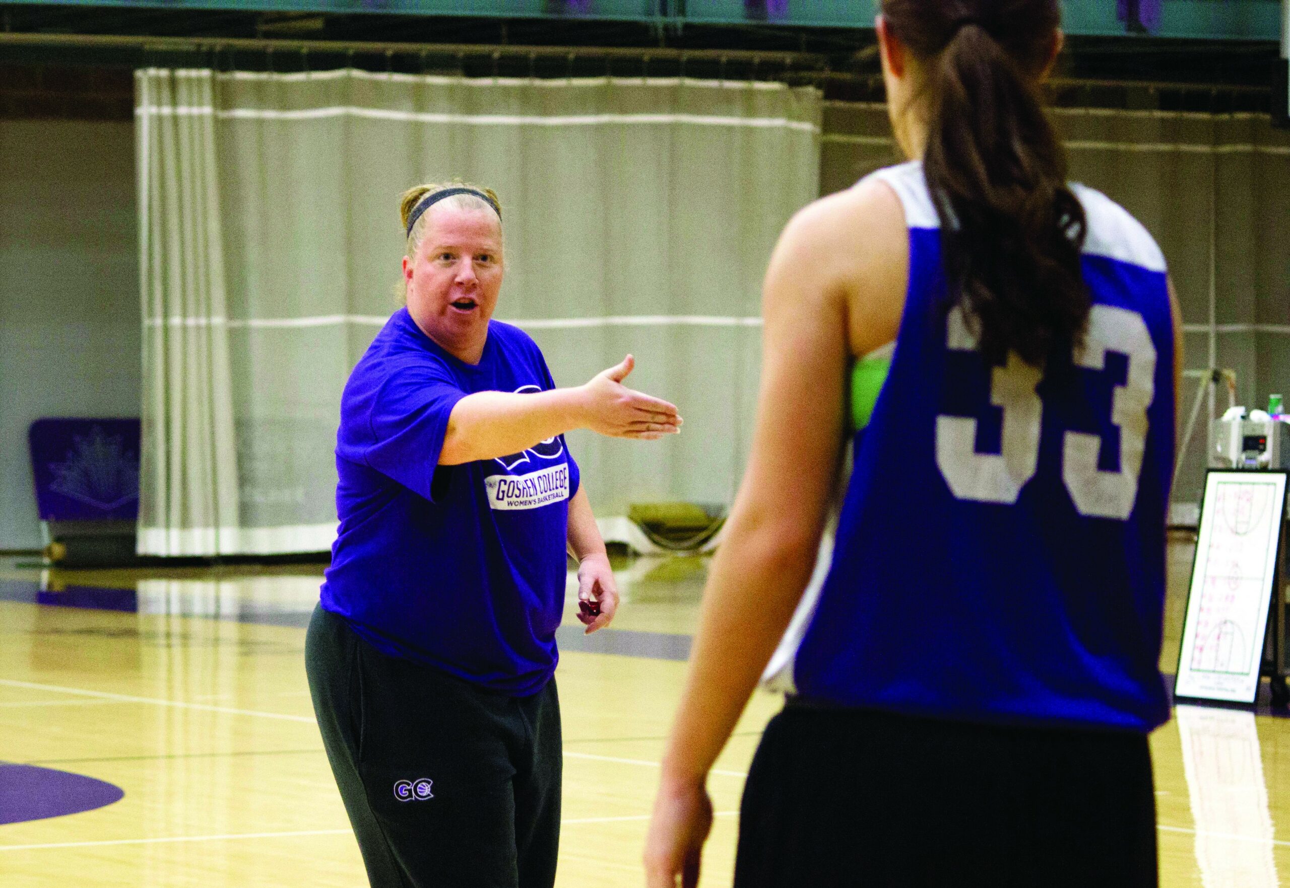 Stephanie Miller talks and gestures to a Goshen player on the women's basketball team. The player is wearing the number "33"