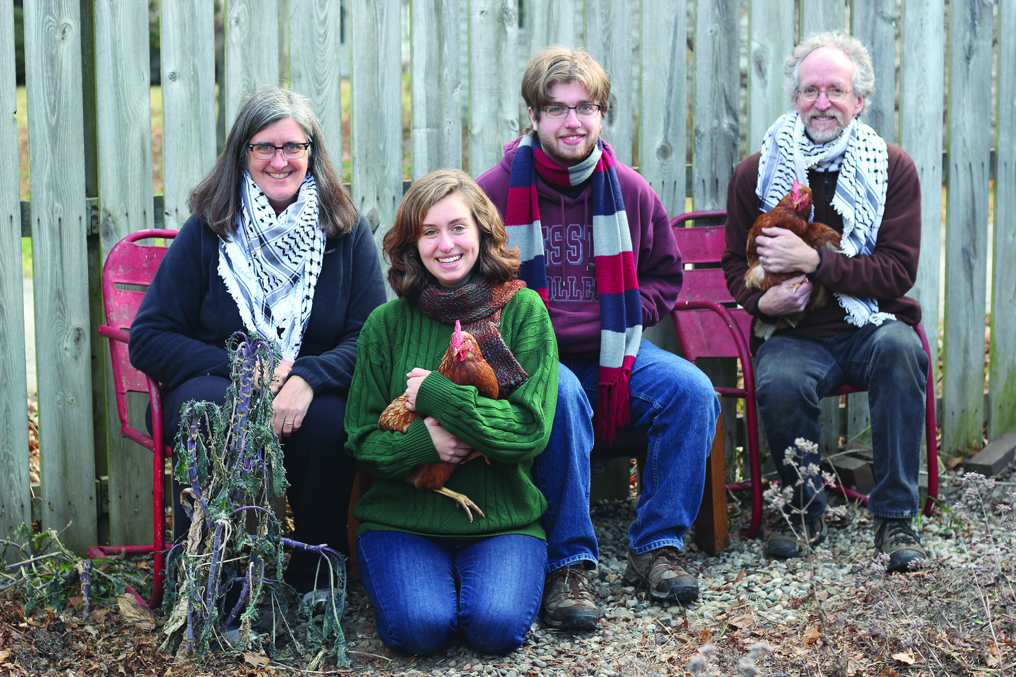 Gwen, Sadie, Si and Les Gustafson-Zook sit on a red bench to pose for a picture with two of their chickens