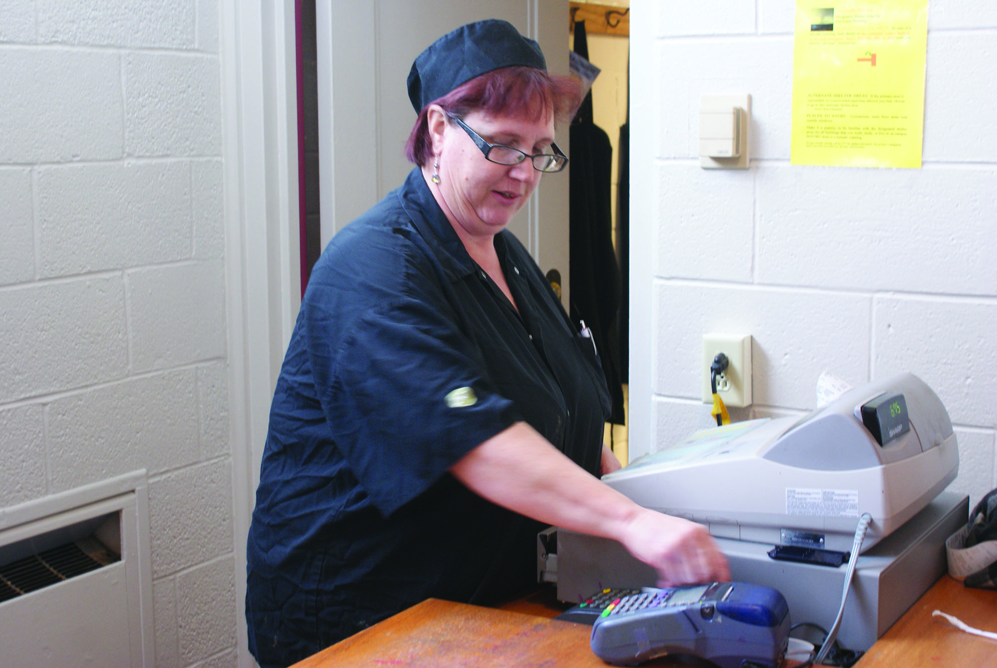 Wearing the black AVI Fresh uniform, Jodi Kuhlman swipes a card at the Leaf Raker cafe cash register