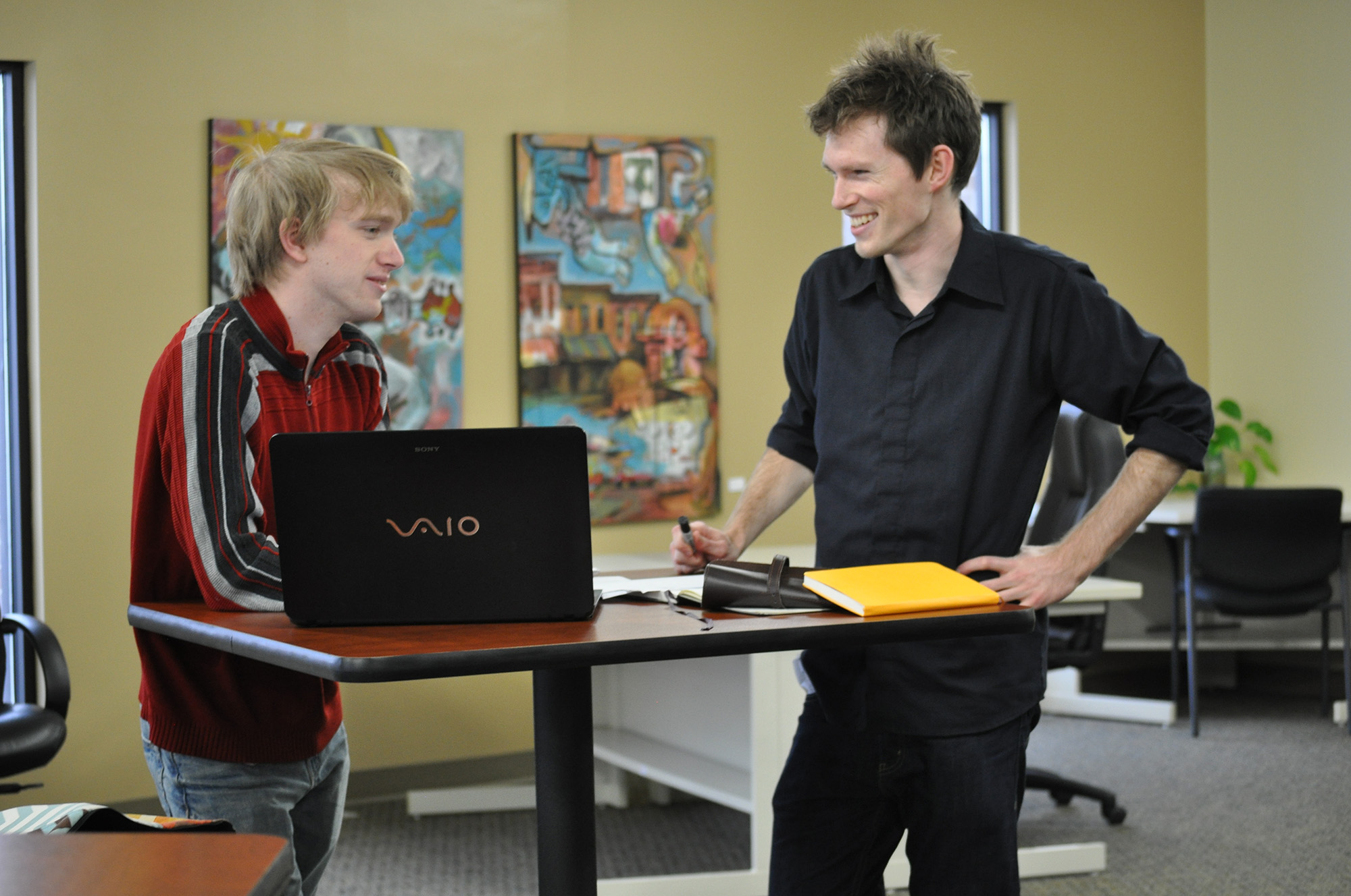 Micah Miller-Eshleman and Alan Smith laugh and work at one of the standing desks in their new studio