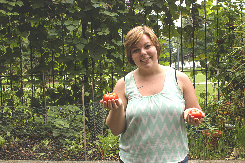 Bekah Shrag holds a tomato in each hand in a garden