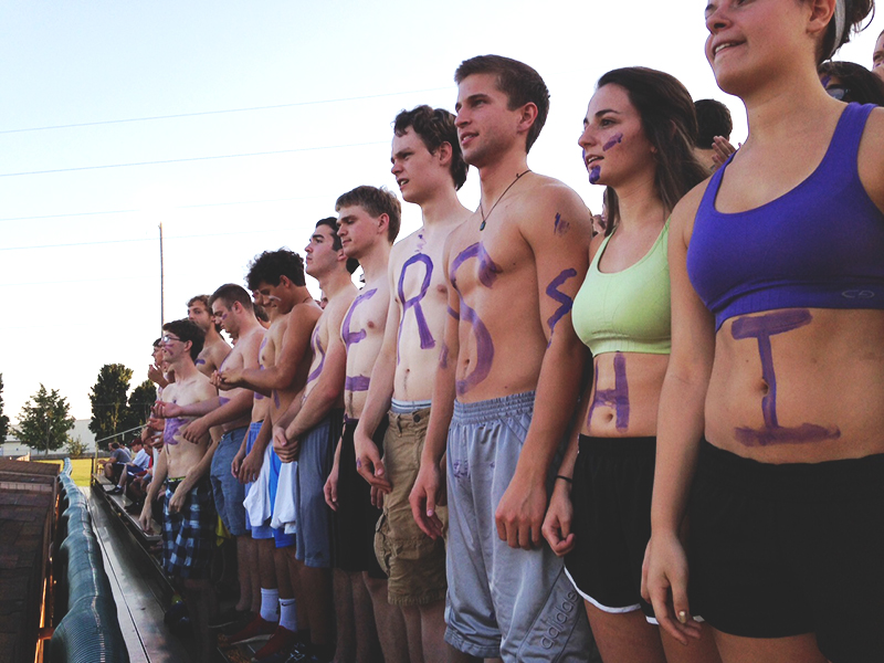Students paint letters on their stomachs and line up to spell a word during a soccer game