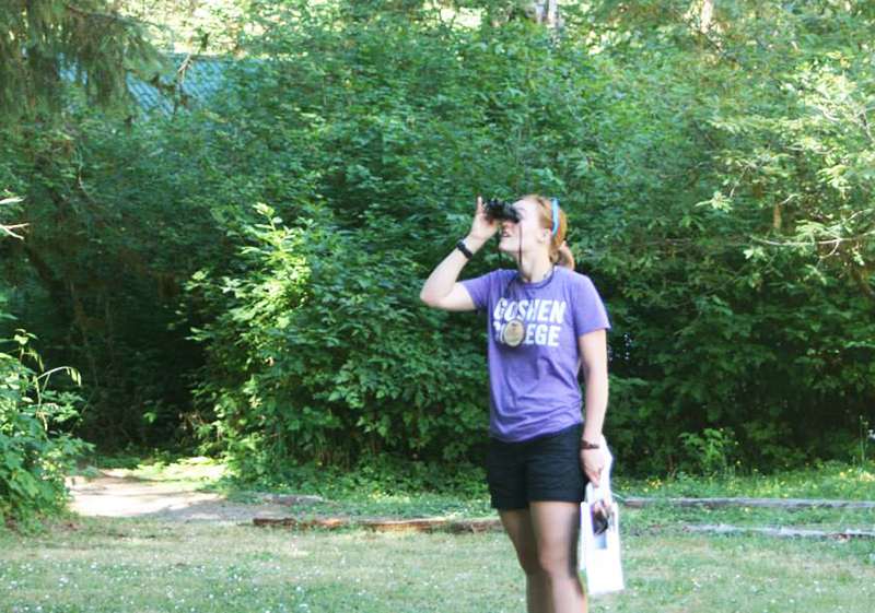 Ellen Conrad looks through a pair of binoculars in the woods
