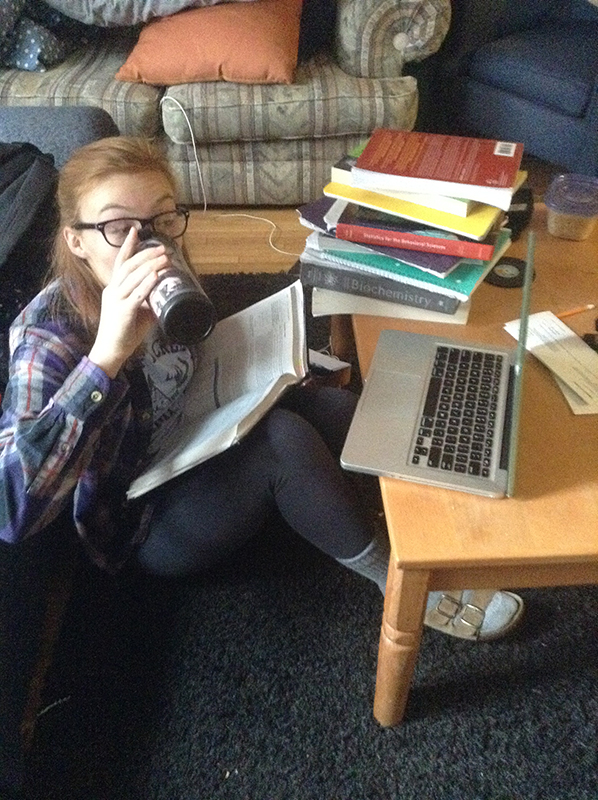 Ellen Conrad sips a drink in the middle of piles of homework and textbooks