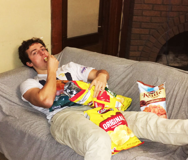 Phil Longenecker lies on a couch while eating several bags of chips