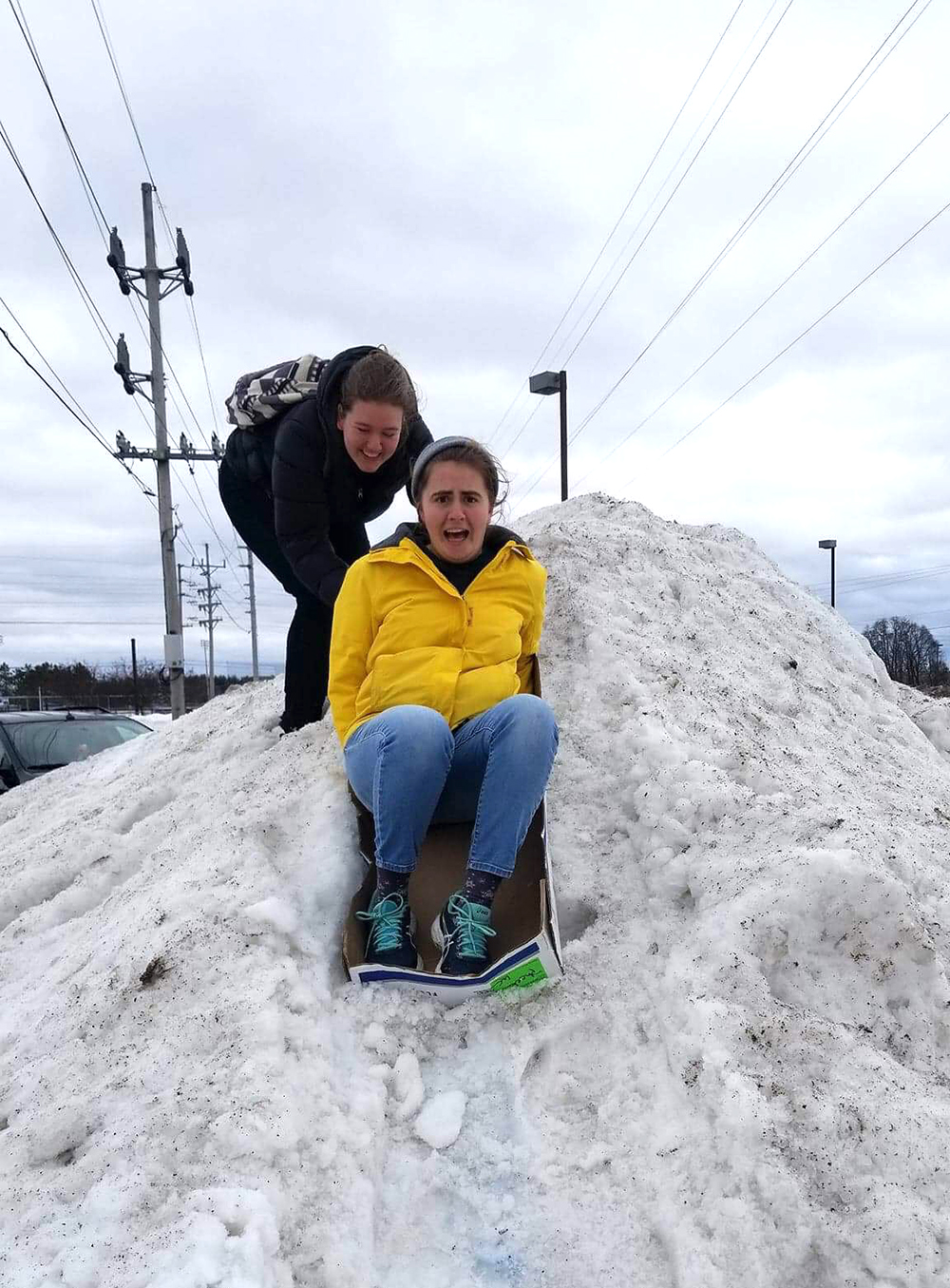A friend pushes Anja Kenagy and her luge down a pile of snow in the parking lot