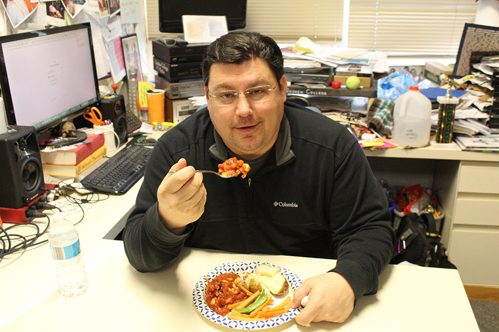 Jason eats a plate of vegan food at the desk in his office