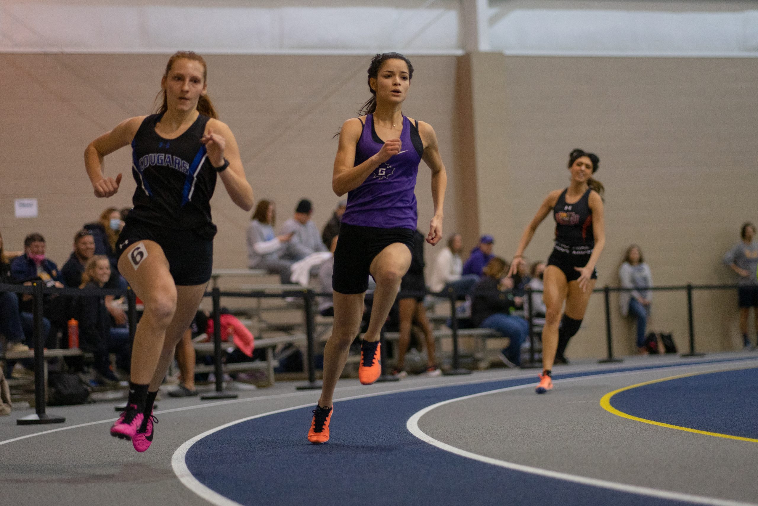 Maria Maldonado and another runner compete in an indoor track event.