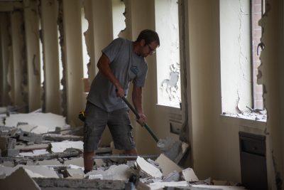 A MDS volunteer swings a sledge hammer at part of the wall as part of demolition.